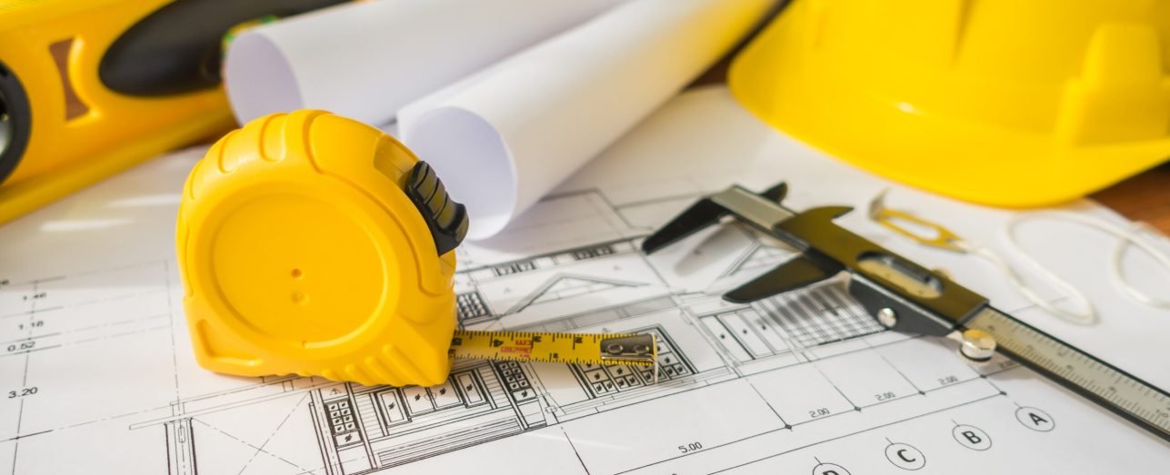 Construction plans with yellow helmet and drawing tools on blueprints